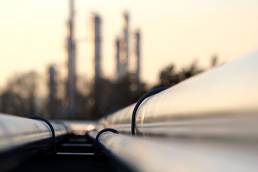 Close-up view of industrial gas pipelines with refinery structures in the background, symbolizing gas line repair and maintenance in industrial facilities.