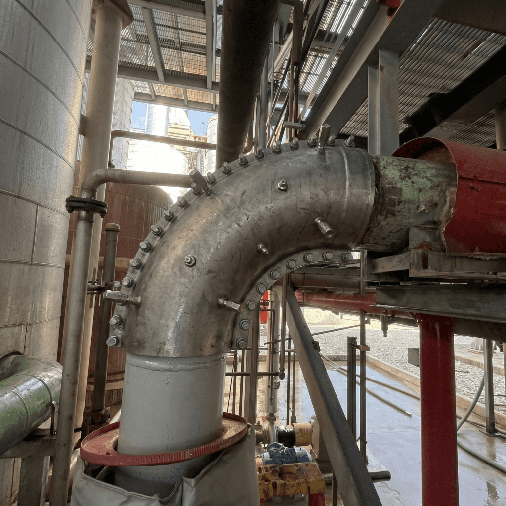 Large industrial pipe elbow with bolted flange connection inside a Pennsylvania processing facility with surrounding piping and equipment